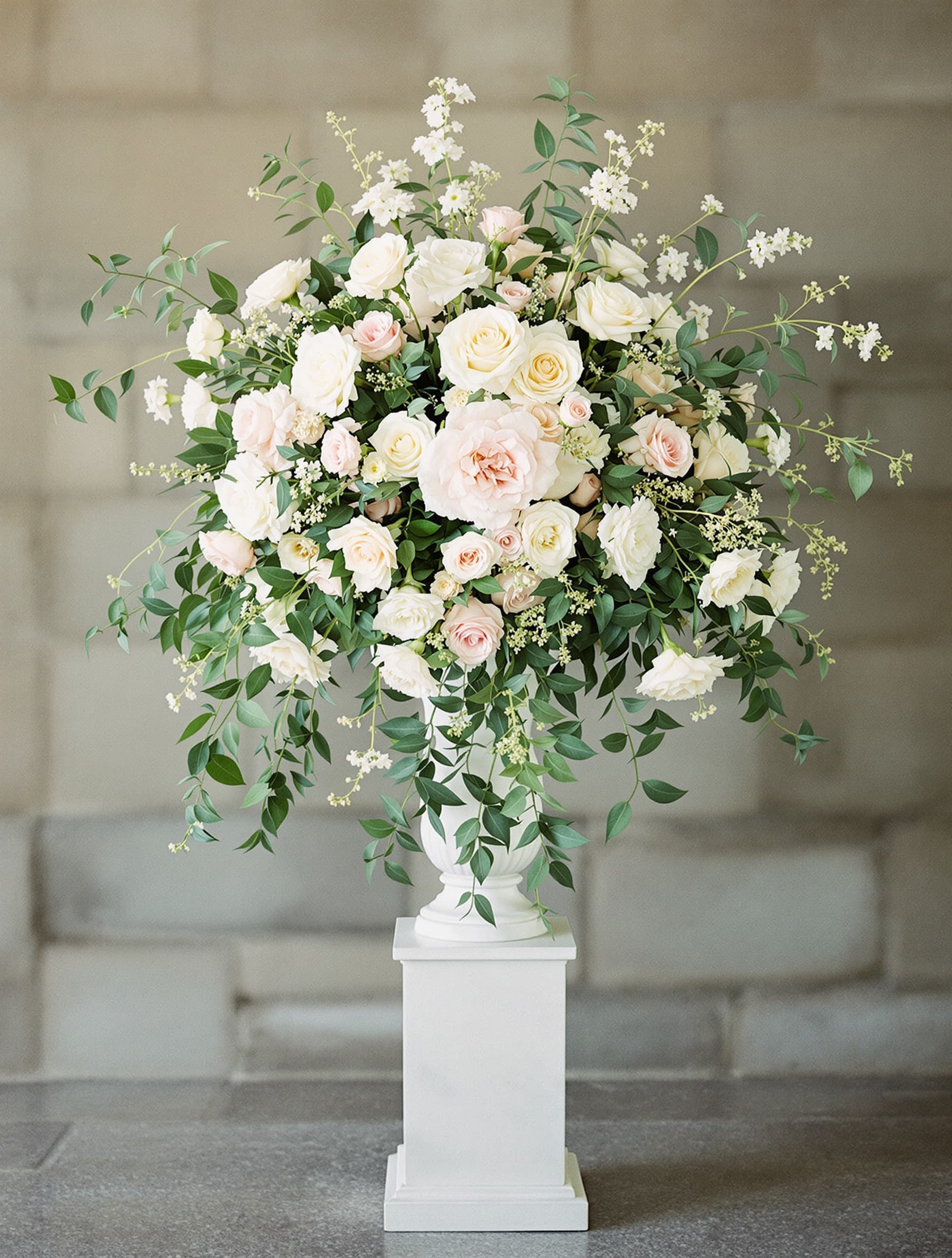 Tall floral pedestal arrangement of cream and blush blooms with cascading greenery