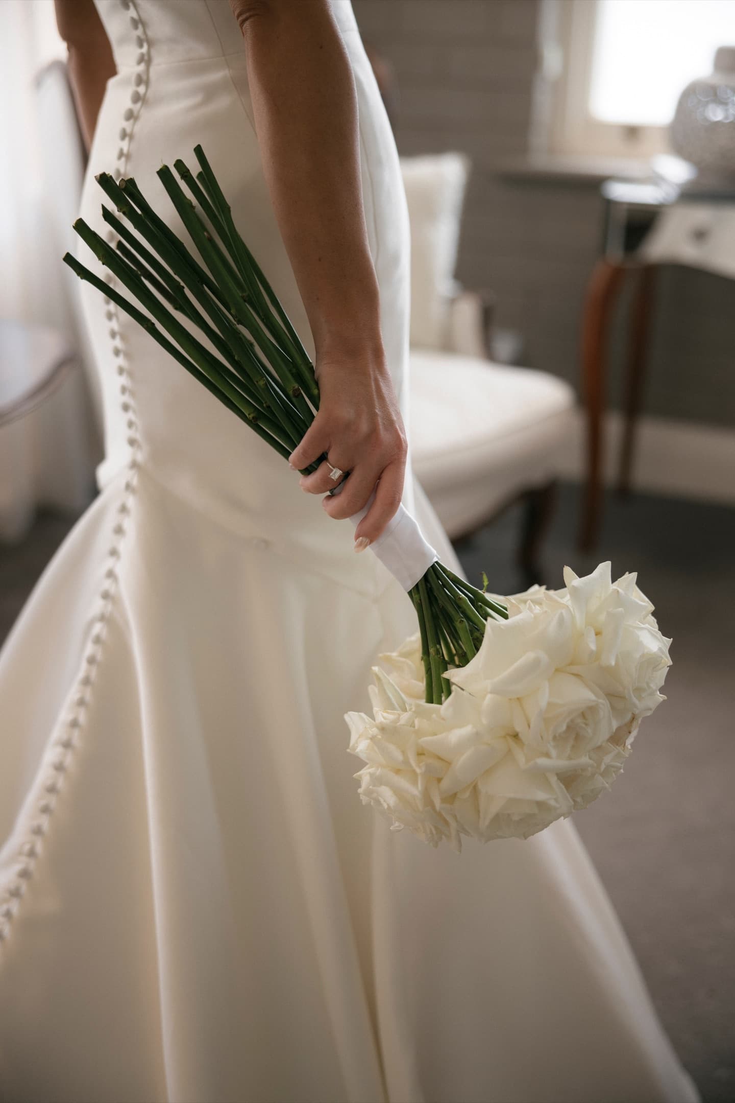 Bride holding a dome bouquet of long-stem white roses at her side, stems wrapped in satin ribbon, designed by La Fleur Botanica