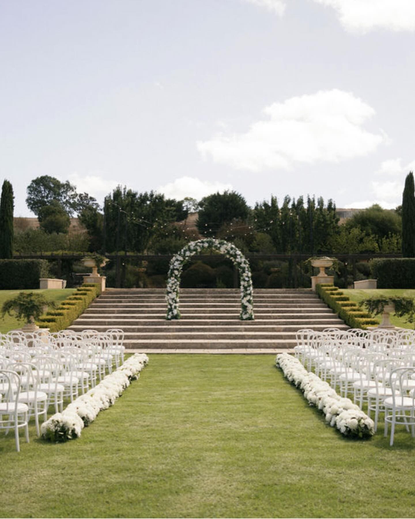Garden ceremony aisle lined with continuous white flower hedge installation at Mandalay House and Garden